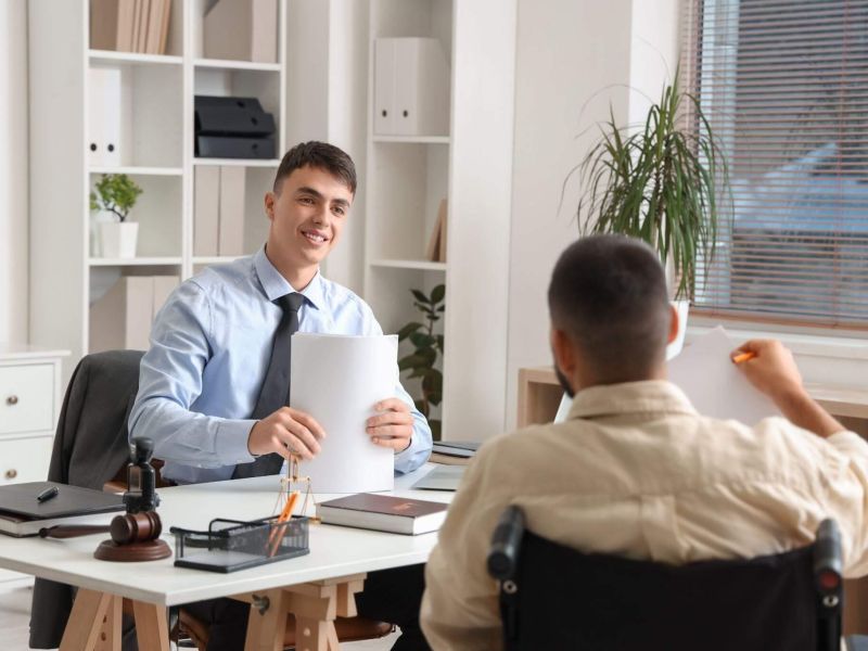a man sitting at a desk in front of a man holding a piece of paper