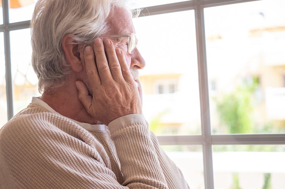 elderly man staring out of the window looking worried.