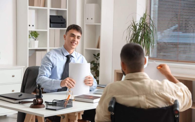 a man sitting at a desk in front of a man holding a piece of paper