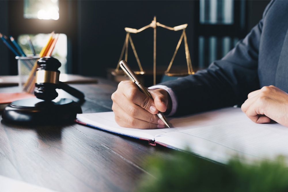 Lawyer writing at desk with gavel and scales of justice, focusing on legal documents.