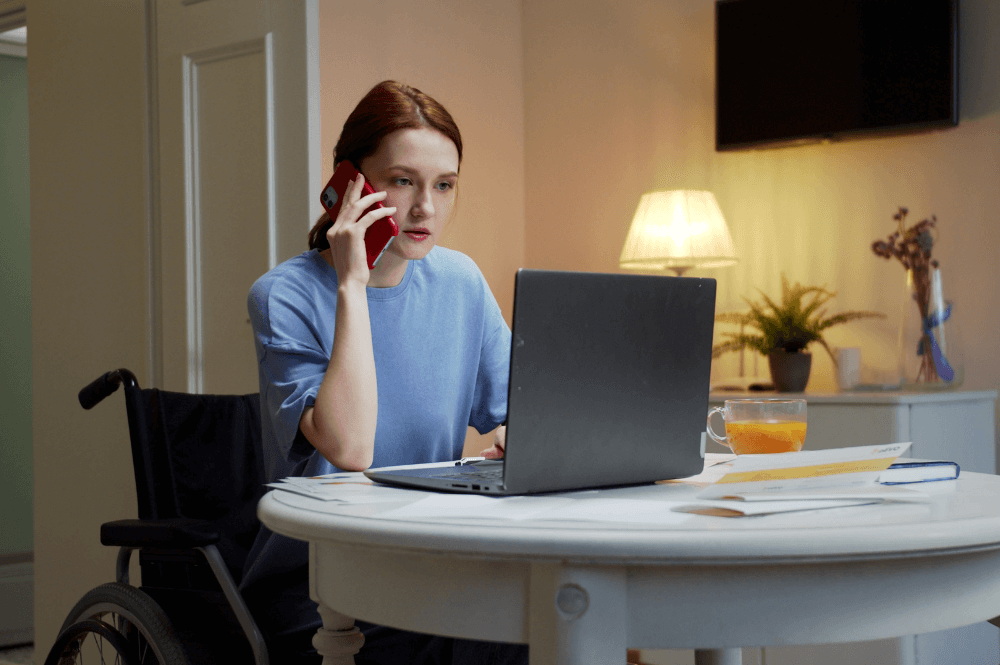 woman in a wheelchair on her laptop while taking a call on her cellphone