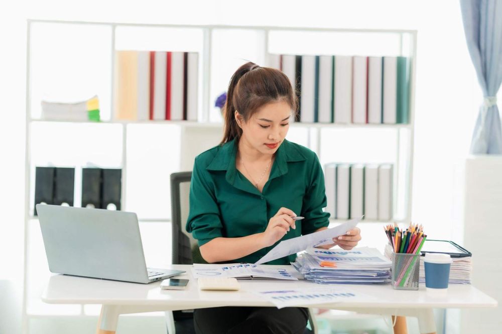 a woman sitting at a desk with a laptop and papers