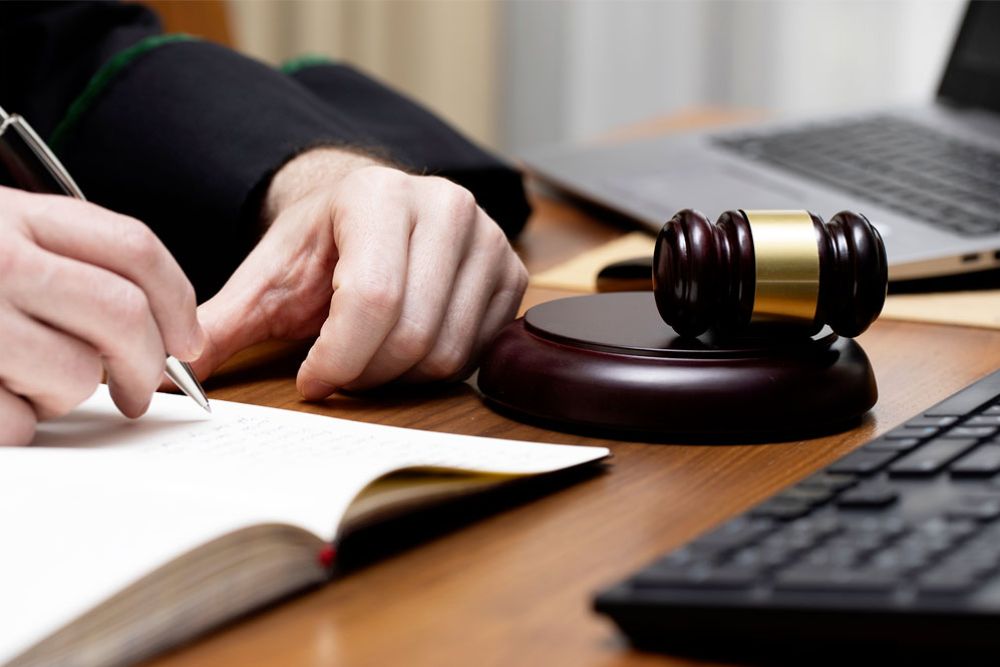 Judge writing in notebook with gavel and laptop nearby on desk. Legal decision-making concept.