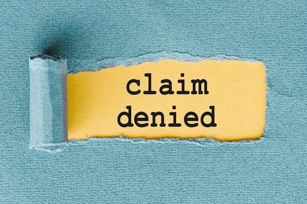Torn paper revealing claim denied text on yellow background, symbolizing denial or rejection.