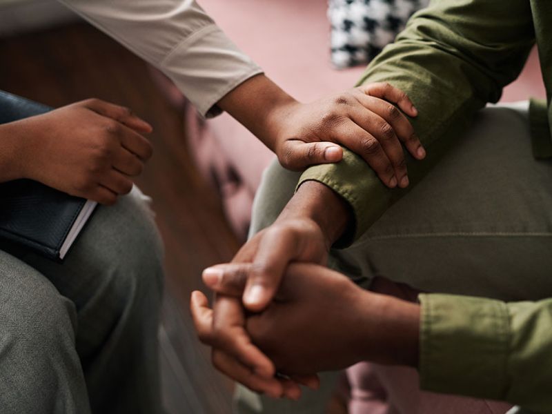 Two people in a comforting gesture with hands touching during a supportive conversation in a cozy setting.