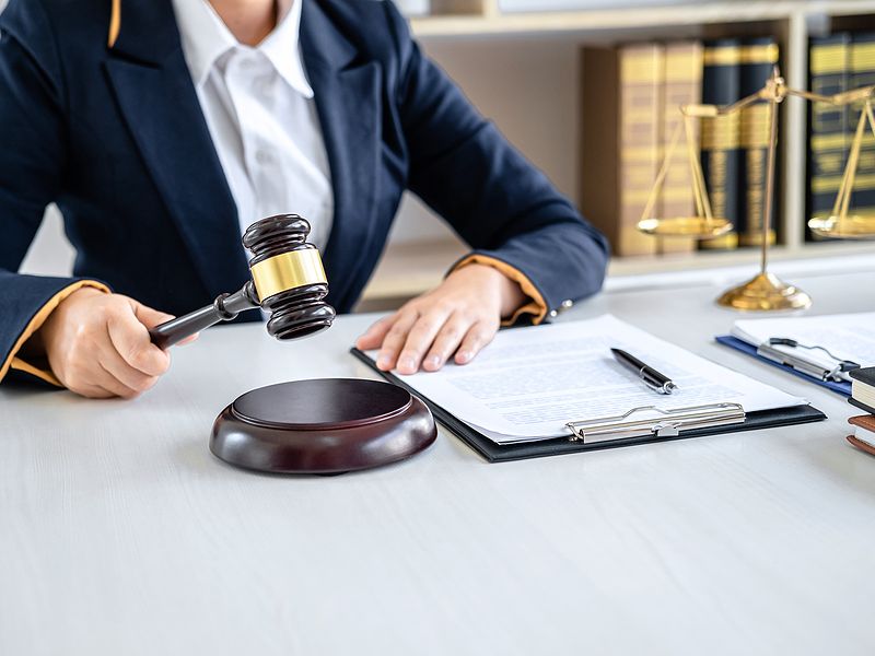 Lawyer in office holding gavel, legal documents on desk, golden scales in background.