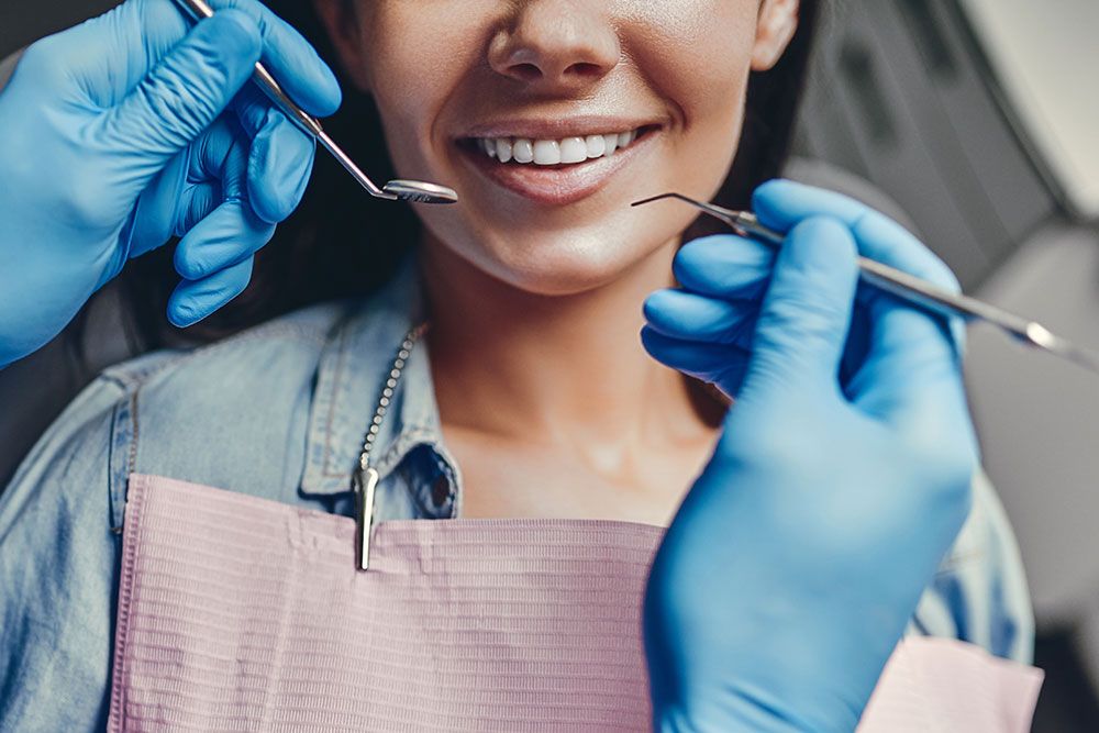 Smiling woman at dentist office getting dental checkup, close-up of dentist tools and patient's smile.