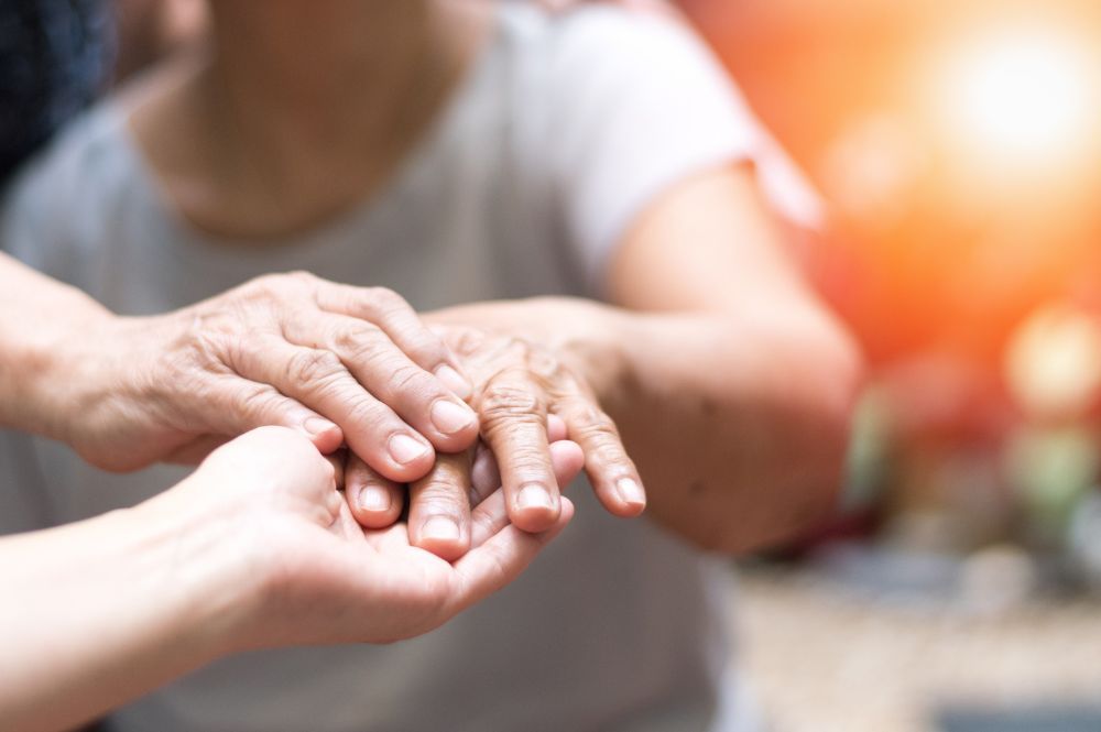 Elderly hands resting in younger hands, displaying care and connection in a warmly lit, intimate setting.