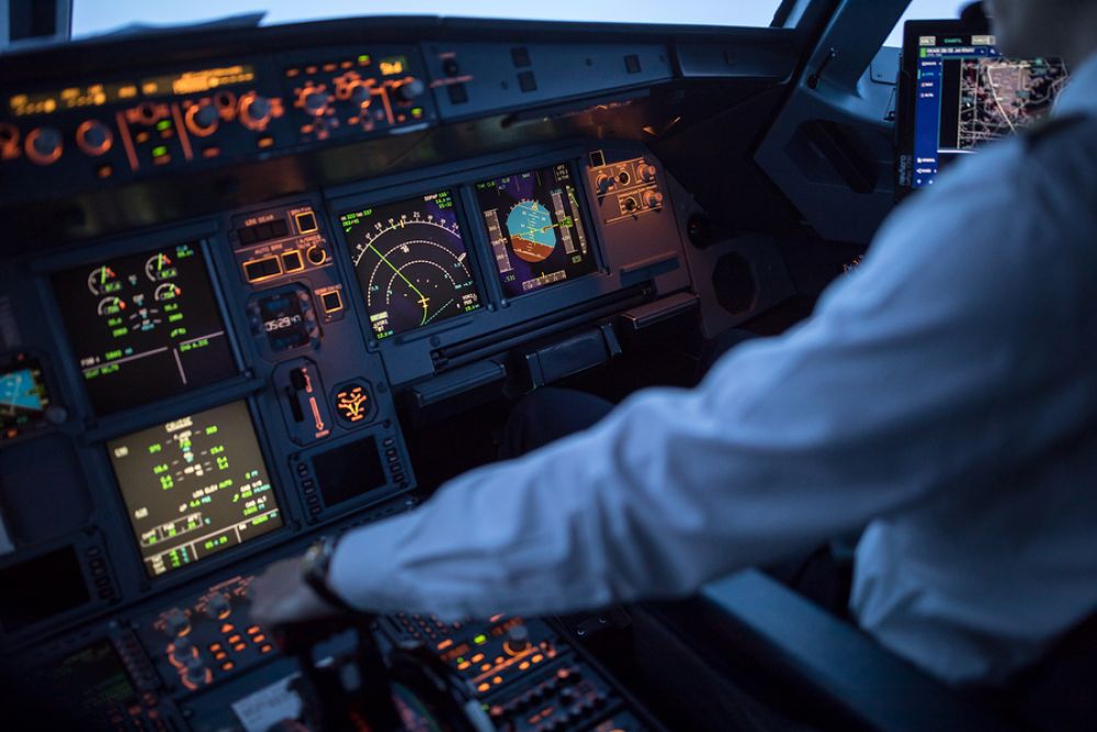 Pilot operating an airplane cockpit with illuminated control panels at dusk.