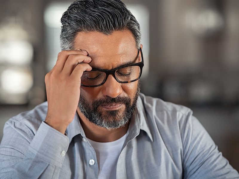 Man with glasses experiencing stress or headache, holding head.