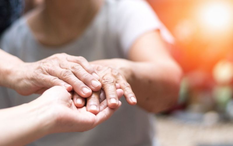Elderly hands resting in younger hands, displaying care and connection in a warmly lit, intimate setting.