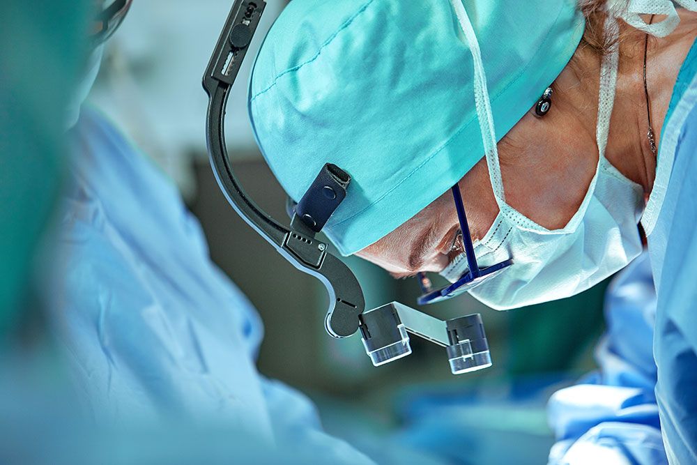 Surgeon focused during operation, wearing magnifying glasses and scrubs, performing a precise surgical procedure.