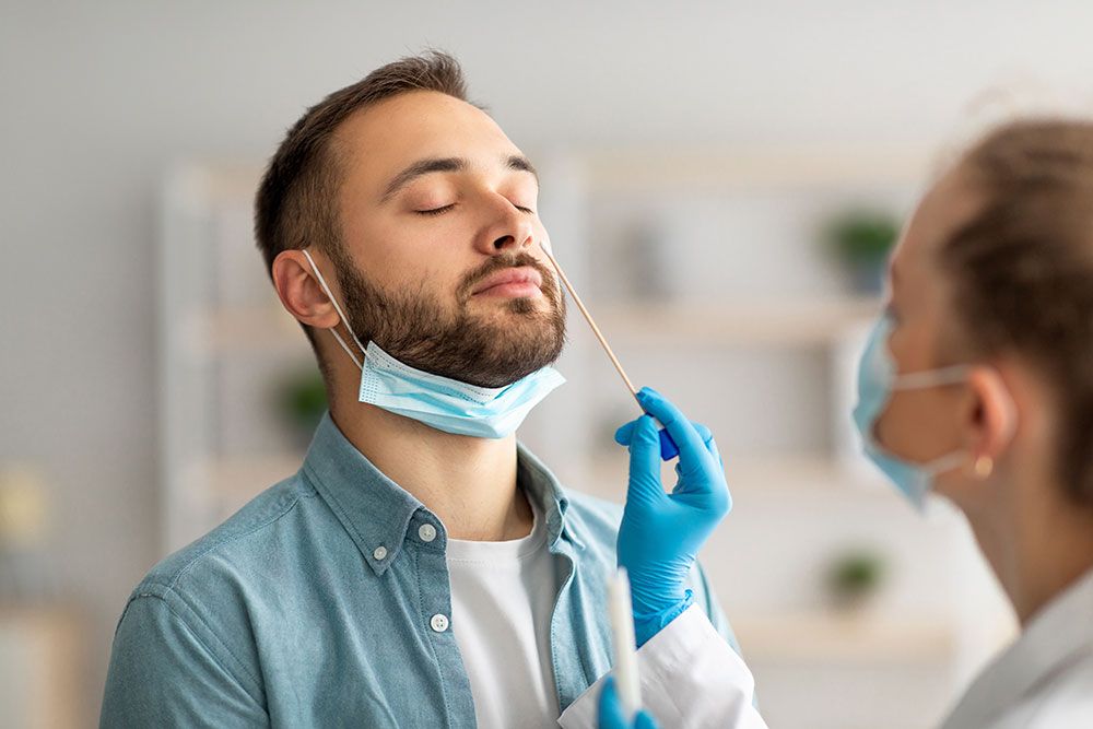 Healthcare worker performing nasal swab test on patient during COVID-19 screening, both wearing protective masks.
