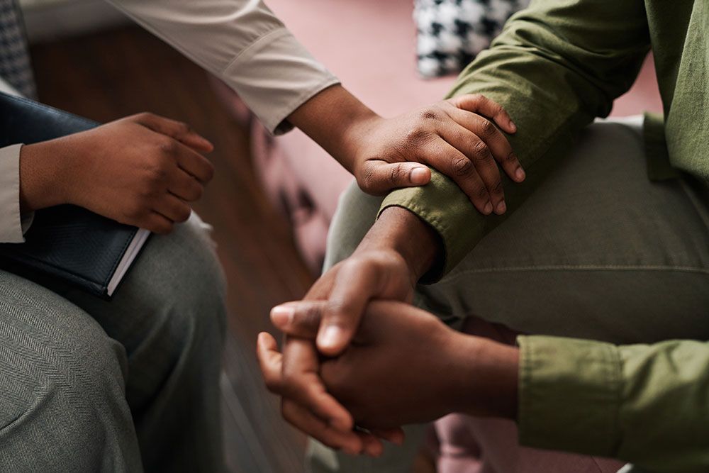 Two people in a comforting gesture with hands touching during a supportive conversation in a cozy setting.