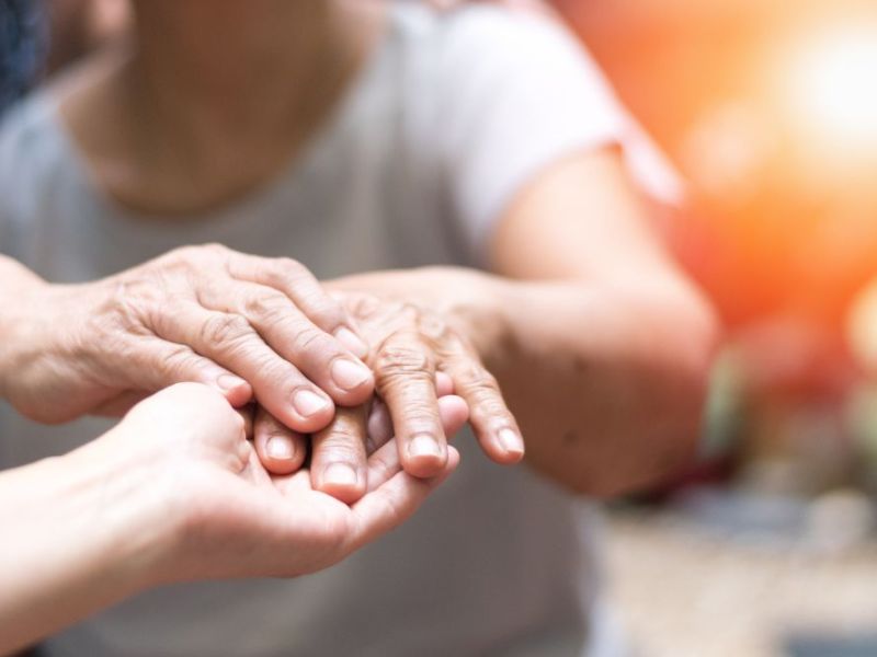 Elderly hands resting in younger hands, displaying care and connection in a warmly lit, intimate setting.