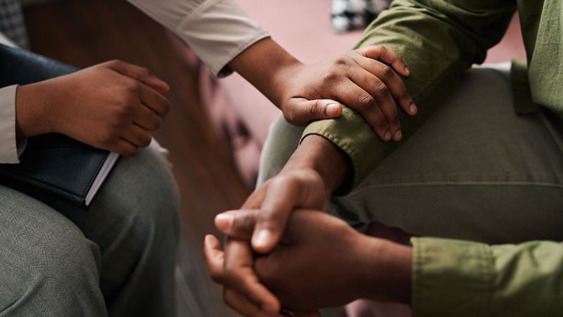 Two people in a comforting gesture with hands touching during a supportive conversation in a cozy setting.