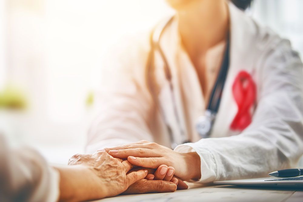 Doctor comforting patient, holding hands in a medical office, with a stethoscope and pink ribbon symbolizing care.