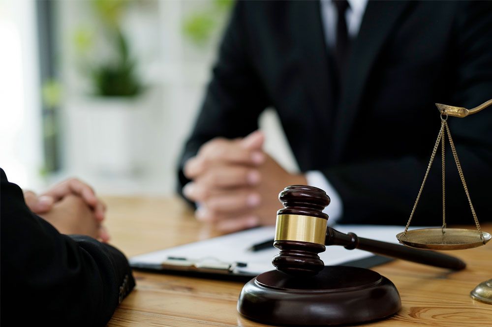 an attorney sitts across the desk from a client. A gavel sits resting on the lawyers desk