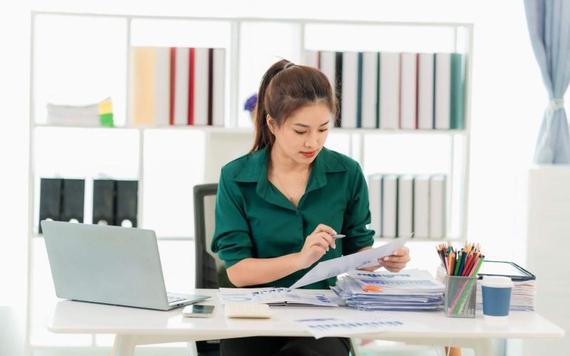 a woman sitting at a desk with a laptop and papers