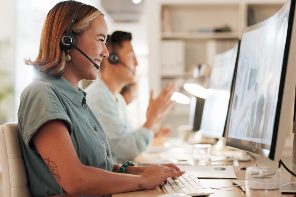 Smiling customer service agents using headsets and computers in a modern office environment.