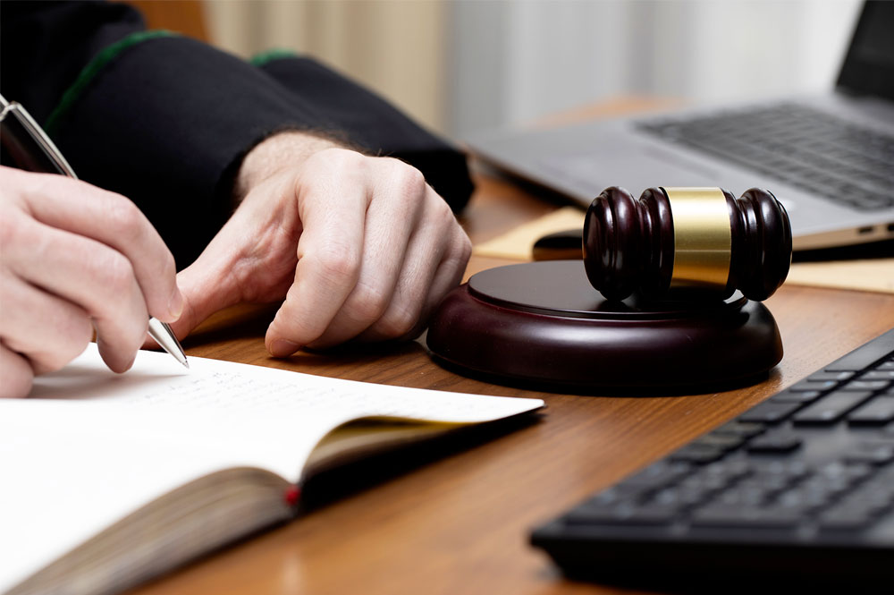 Judge writing in notebook with gavel and laptop nearby on desk. Legal decision-making concept.