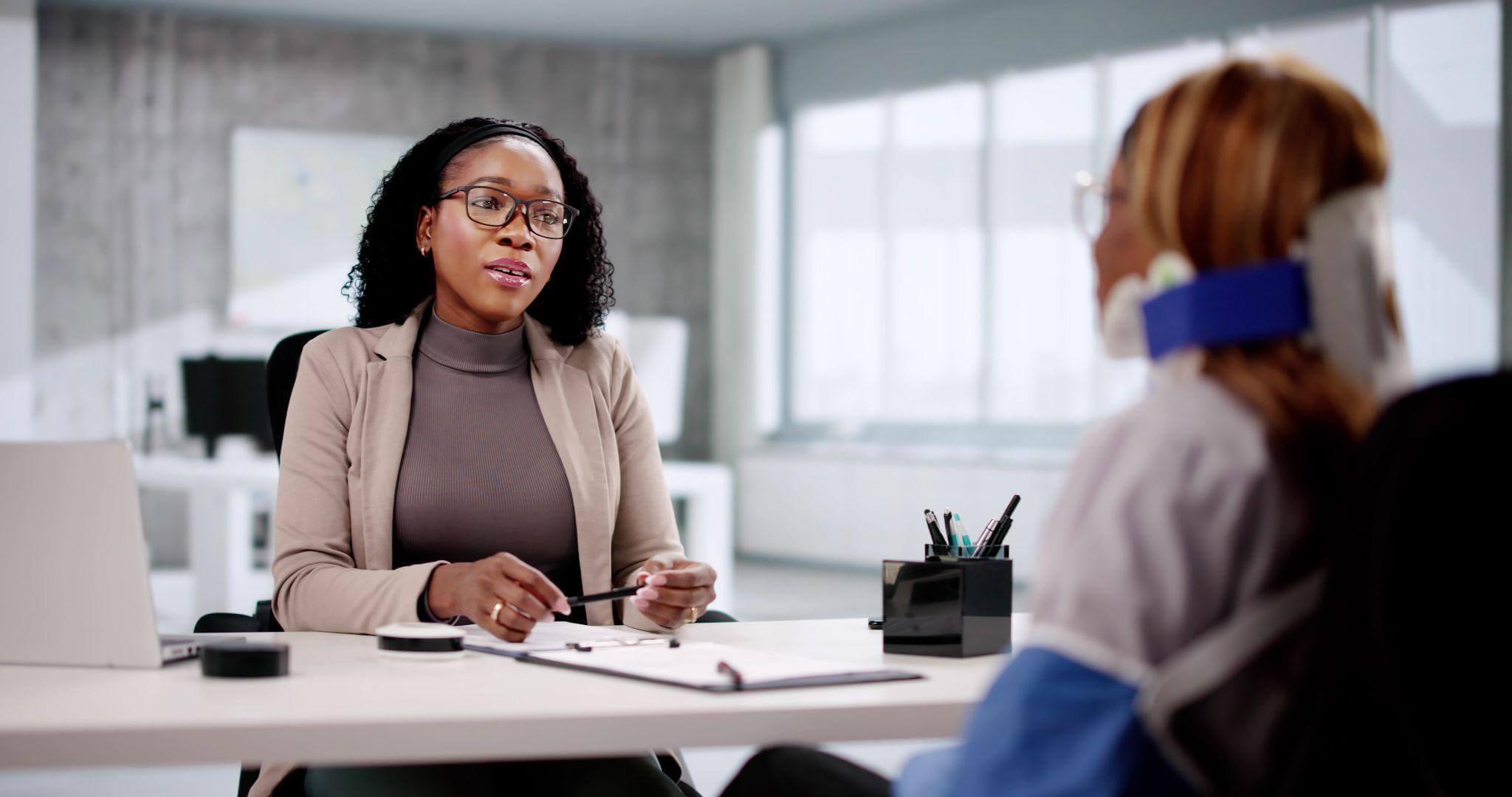 a woman sitting at a desk talking to another woman