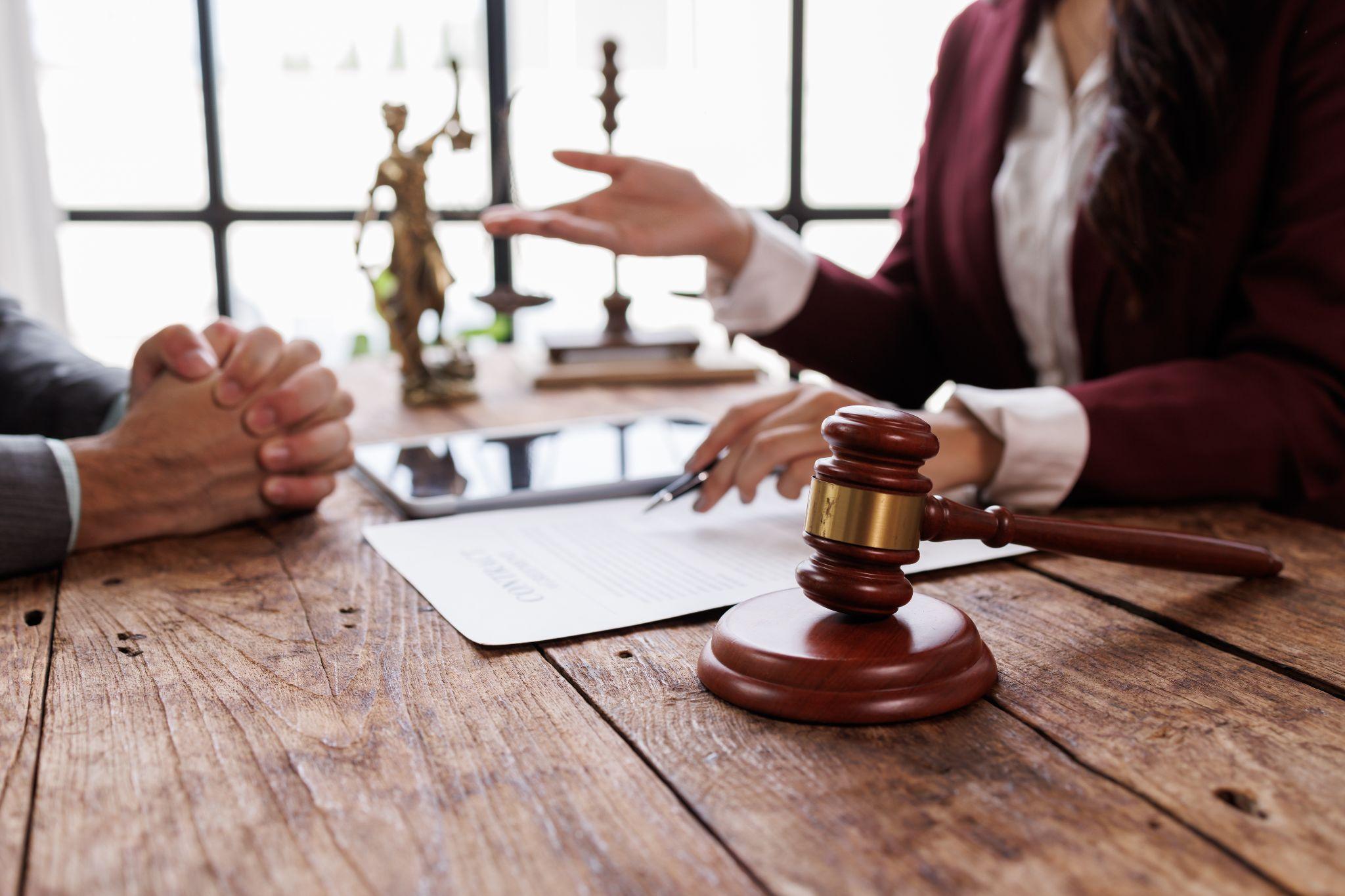 Lawyer and client discussing legal documents at a desk with a gavel and Lady Justice statue.