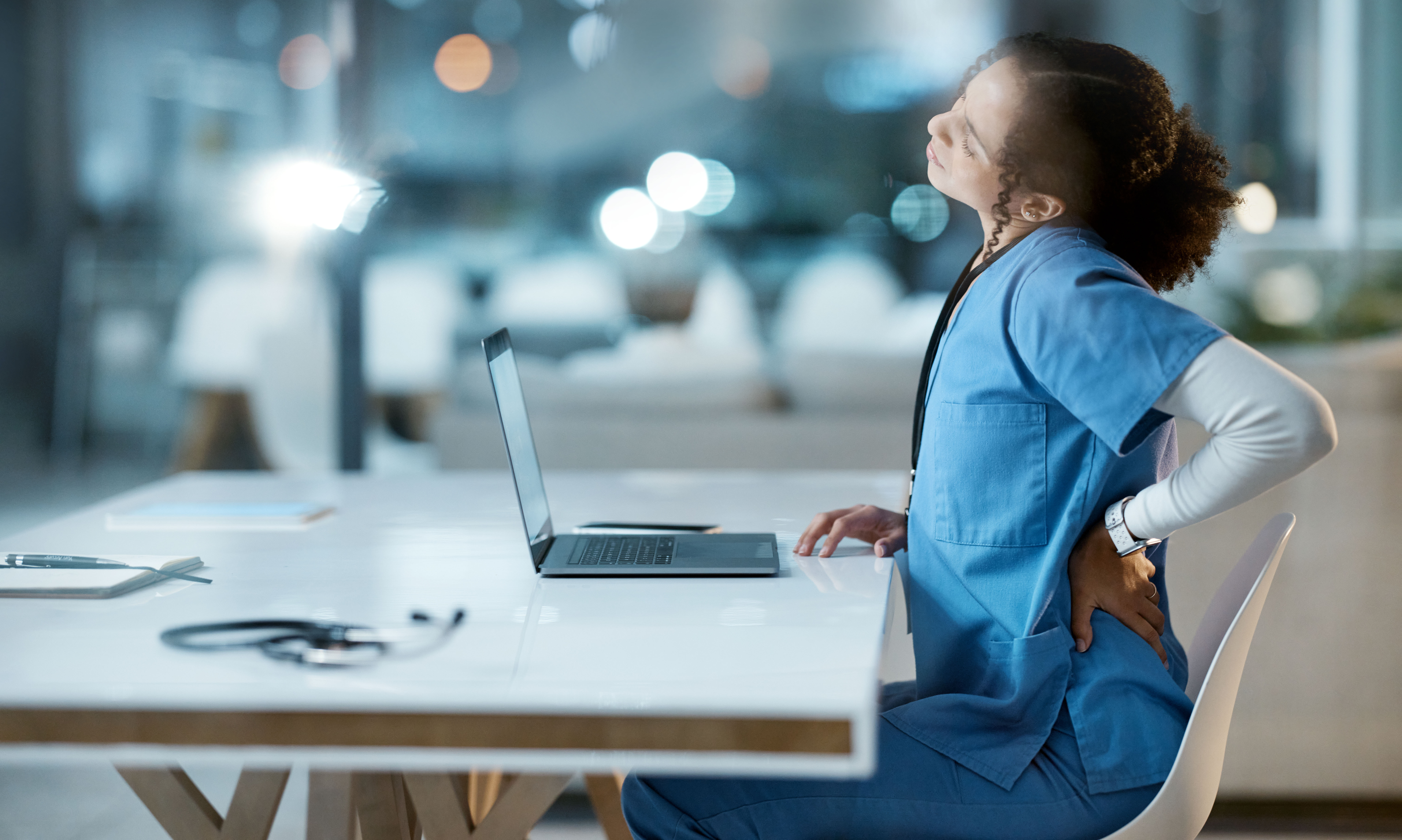 Nurse sitting at table struggling with lower back pain
